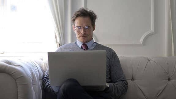 a professionally dressed man sitting on a couch and working on his laptop