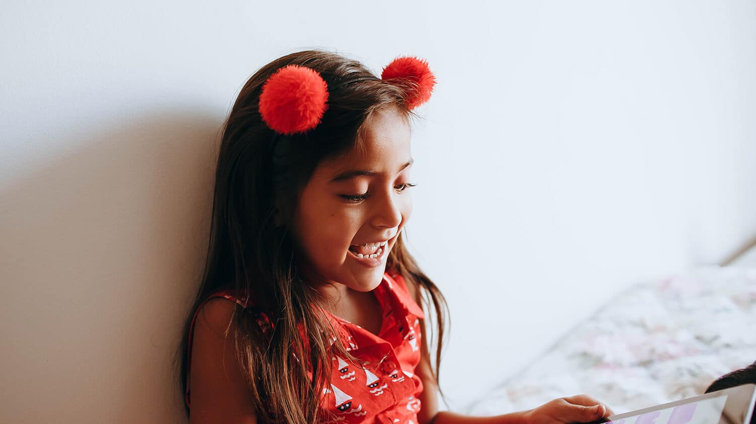 a girl with long brown hair and wearing a red shirt looks at her ipad and smiles