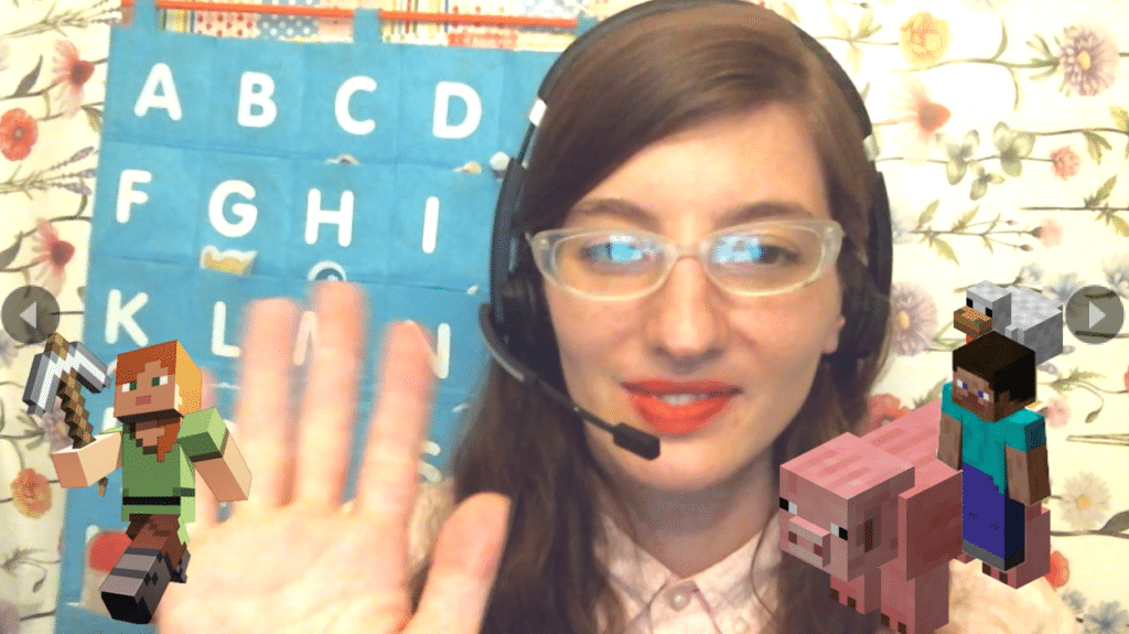 a photo of me teaching in font of my ESL alphabet backdrop and using manycam to add minecraft characters on my screen