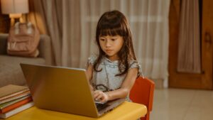 a very young Asian girl sitting and learning online at her laptop