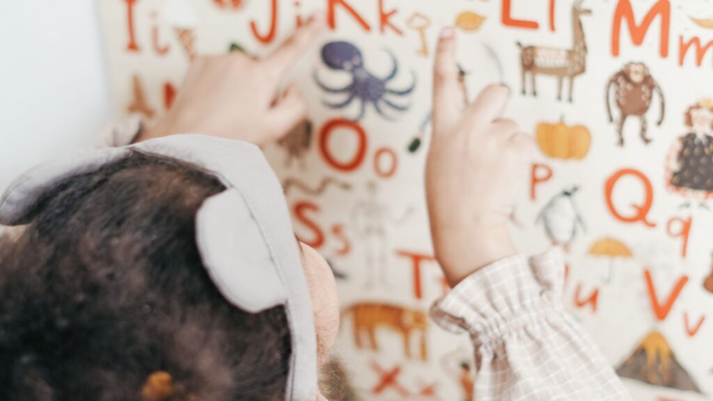 a child looking and pointing at letters of the alphabet and drawings of animals on a board