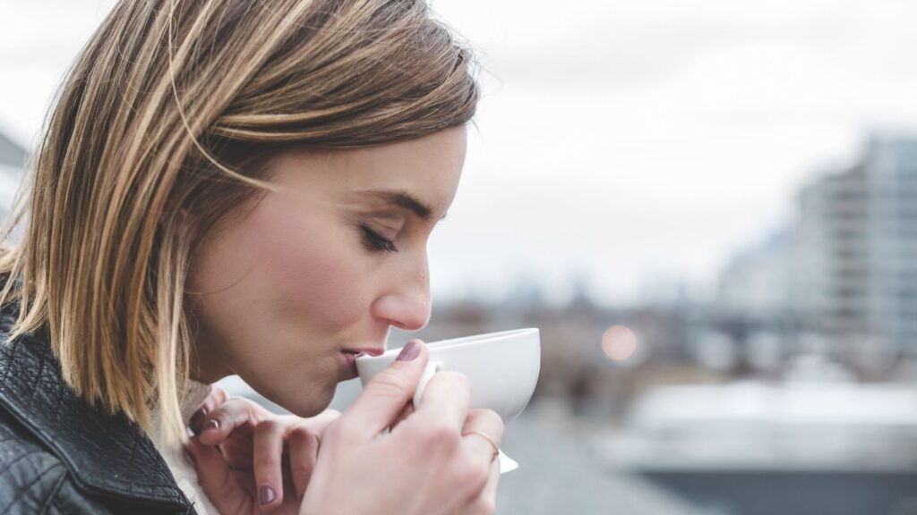 the profile of a woman sipping a white cup of tea while outside on a cloudy day