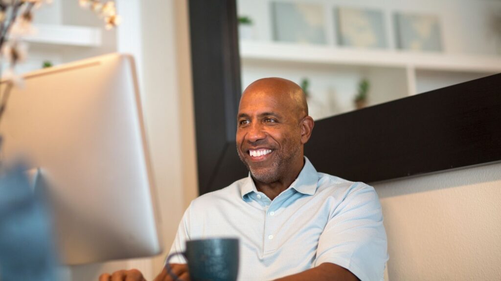an African American man sitting and smiling while facing his desktop 