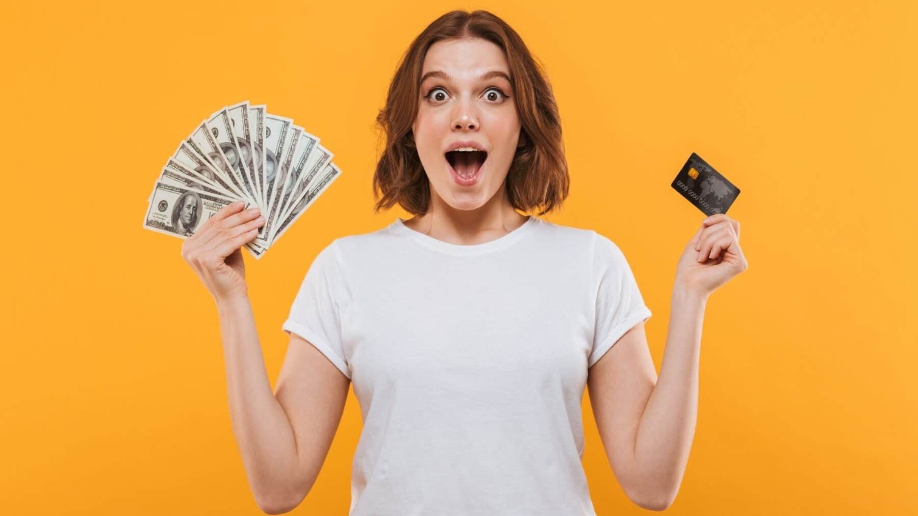 a smiling, young woman with short brown hair in a white Tshirt holding a fan of dollars in one hand and a credit card in the other