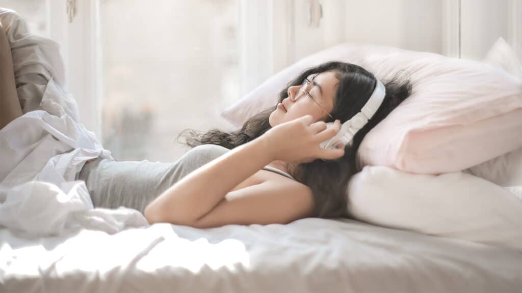 a young woman listening to headphones while lying in bed with her eyes closed