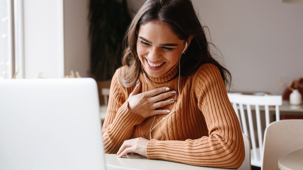 a smiling woman talking to someone on her laptop in a sweater