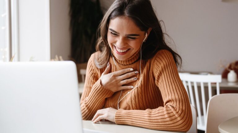 a smiling woman talking to someone on her laptop in a sweater