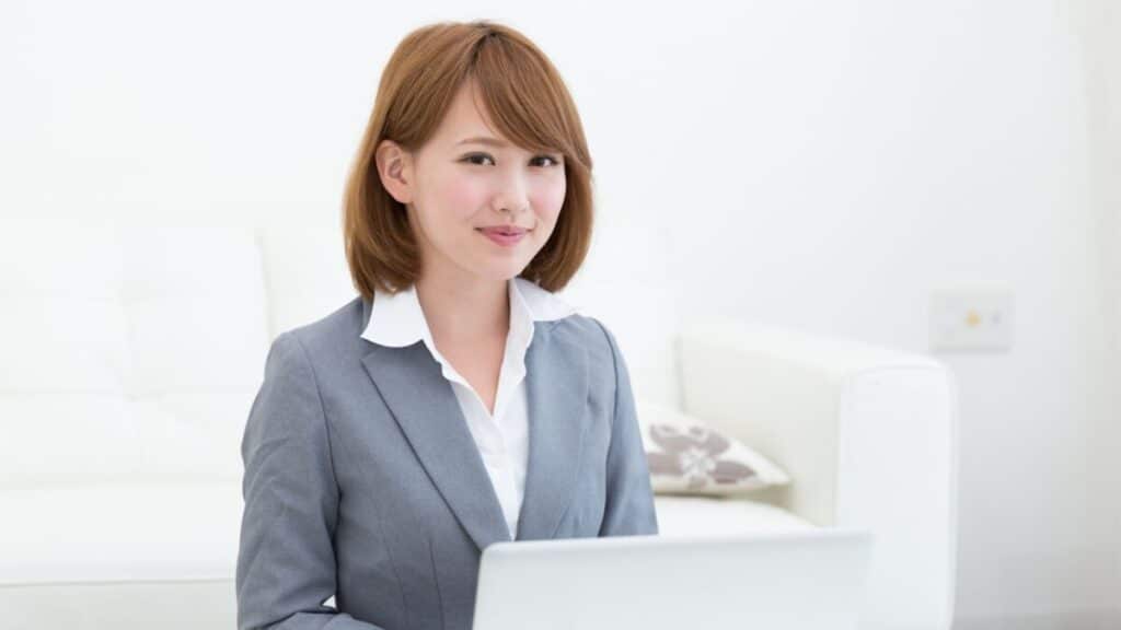 a Japanese woman with a red bob and wearing a suit smiling in front of her laptop 