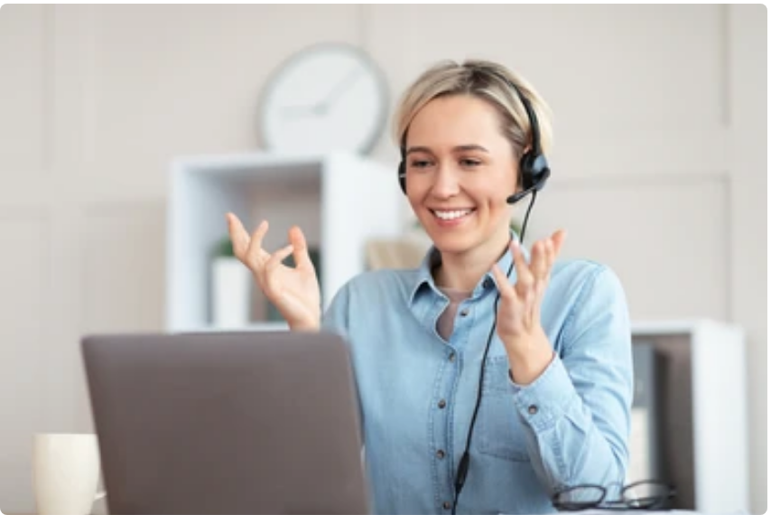 A smiling woman teaching from a laptop using a headset