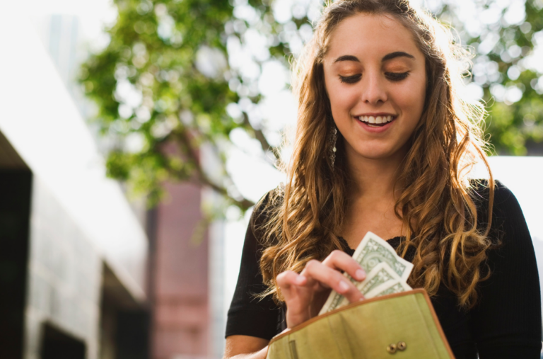 a smiling teenager pulling out her wallet and counting her dollars that she earned from her online job